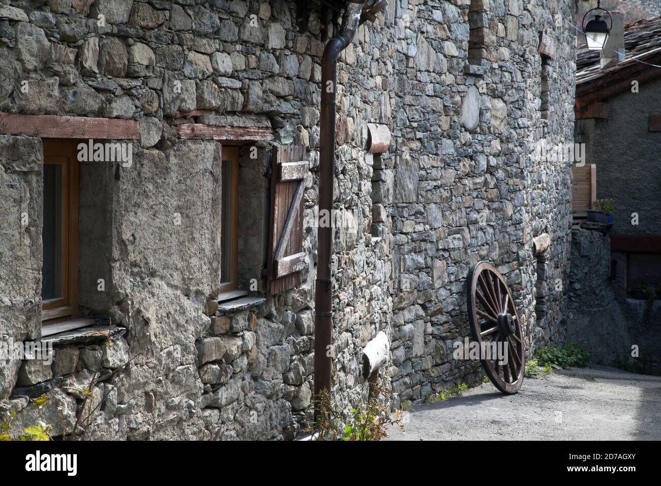 an old wheel resting against the wall and windows of an old stone house in Bonneval-sur-Arc Haute-Maurienne Savoie France Stock Photo