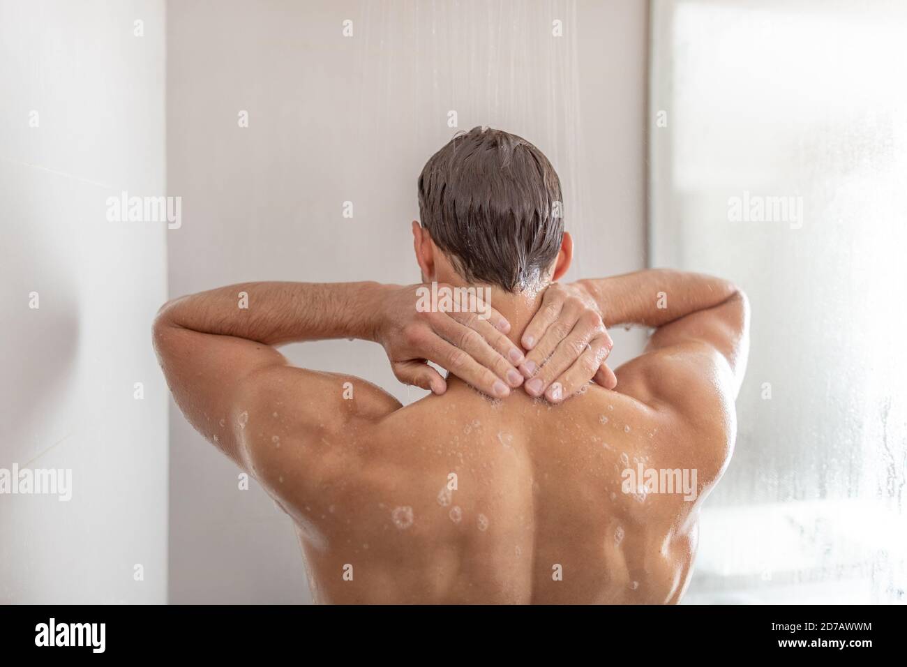 Man taking a shower washing hair under in luxury walk-in hot tub bath. Showering young person touching back of neck at home. Body care male beauty Stock Photo