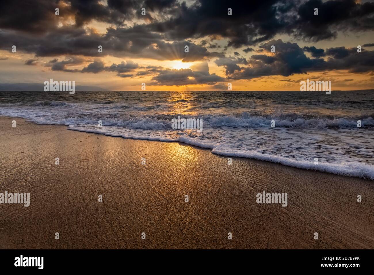 The Sun is Setting on the Ocean Horizon as Sun Rays Burst Through The Clouds Stock Photo