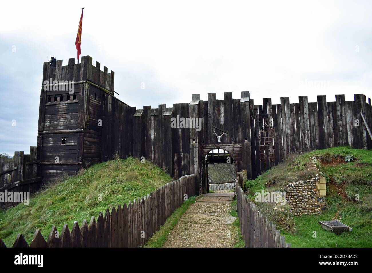 A pathway leads to the wooden castle walls and tower with a red flag at