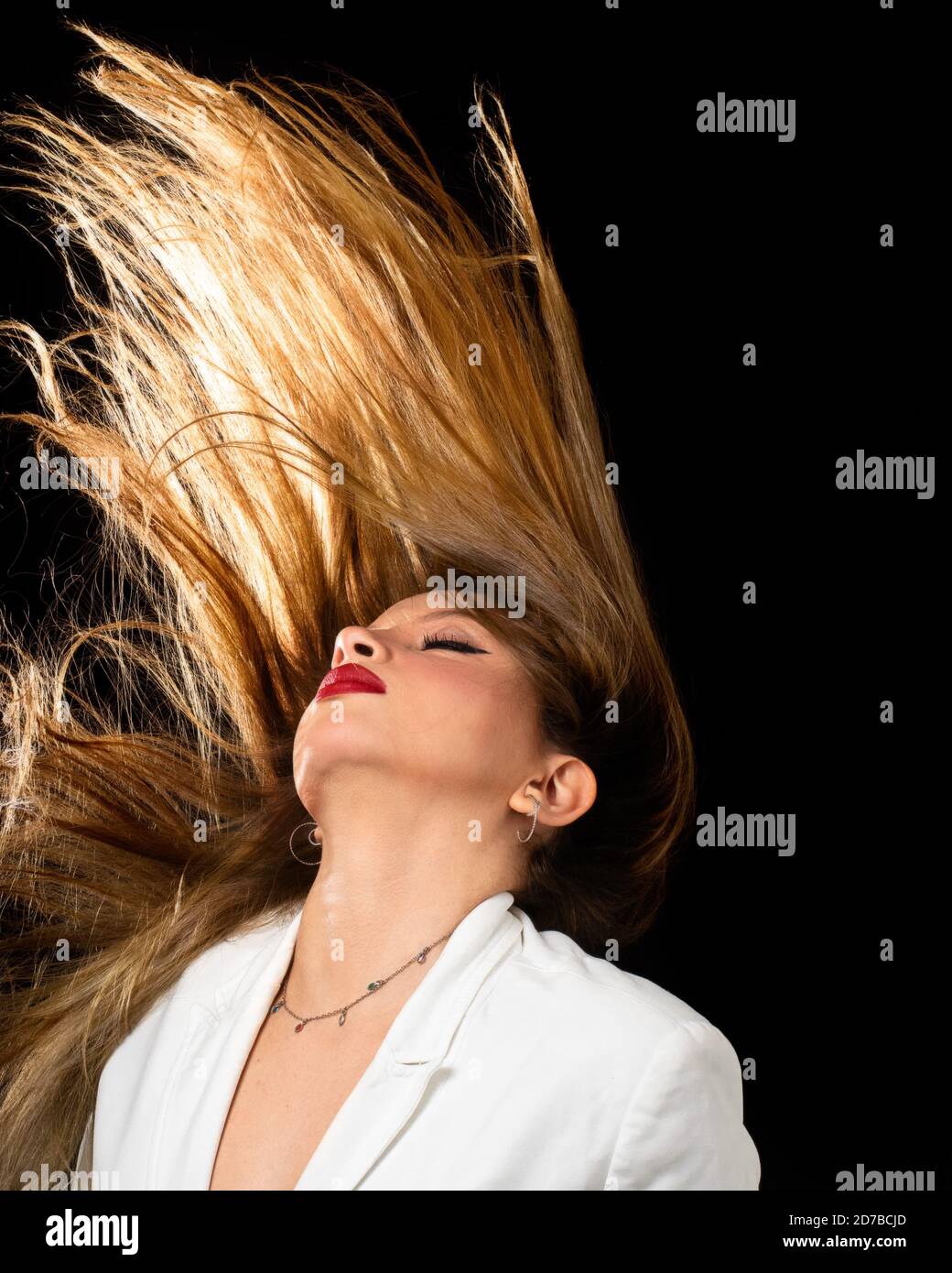 Young woman throwing back hair to the wind backlit studio beauty portrait isolated on black background Stock Photo