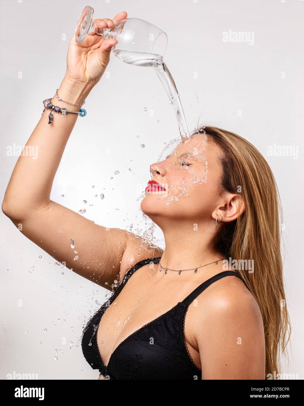 Young caucasian woman splashing a glass goblet of water on herself beauty studio portrait isolated on white background Stock Photo