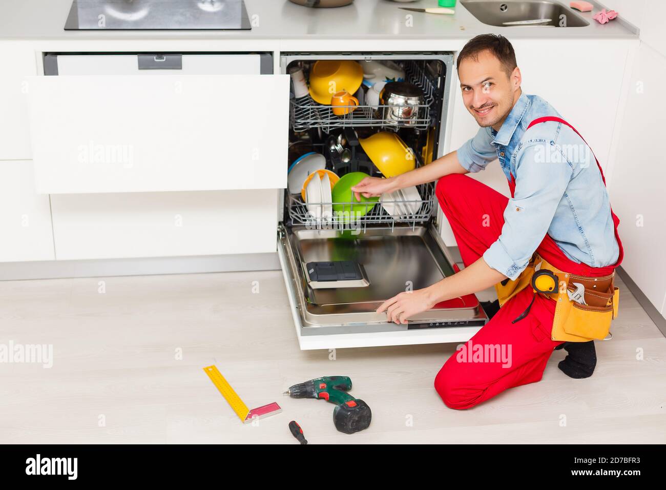 Male technician checking dishwasher with digital multimeter in kitchen