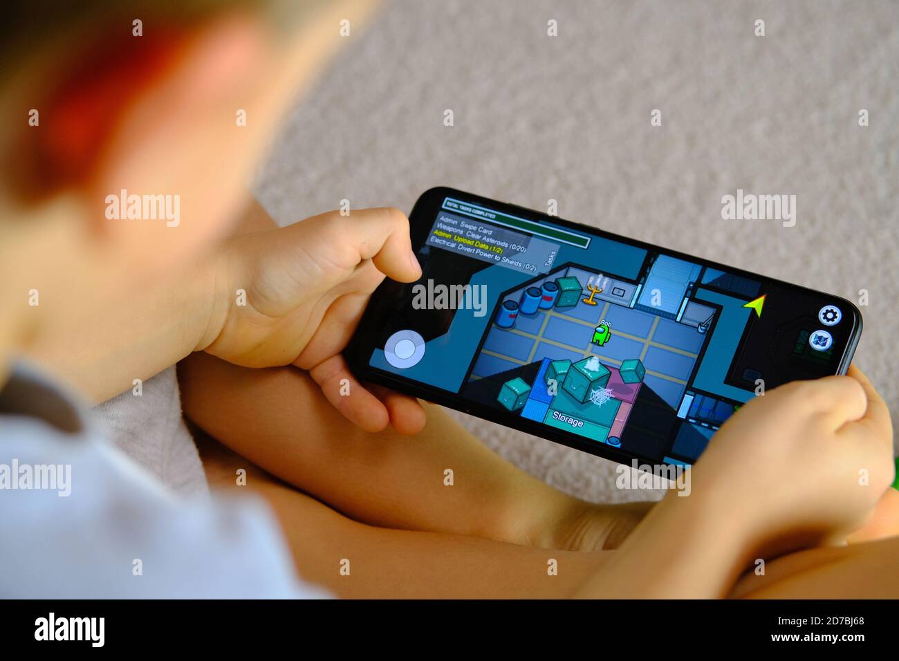 Manchester / United Kingdom - October 21, 2020: Among Us game seen on the smartphone screen and child playing it. New popular app. Stock Photo