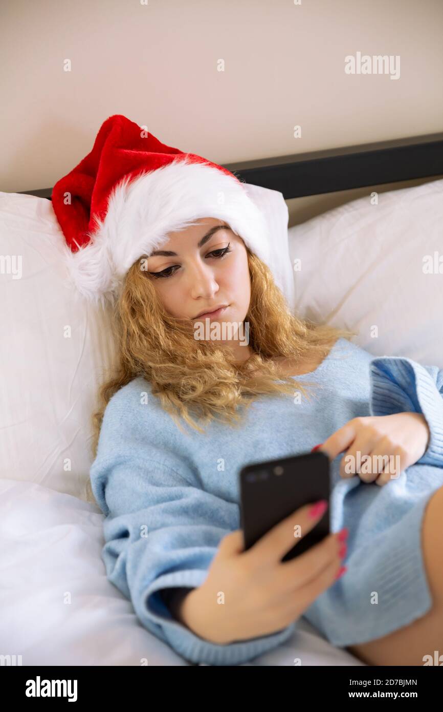 Woman in santa claus red cap with smartphone in  bed. Stock Photo
