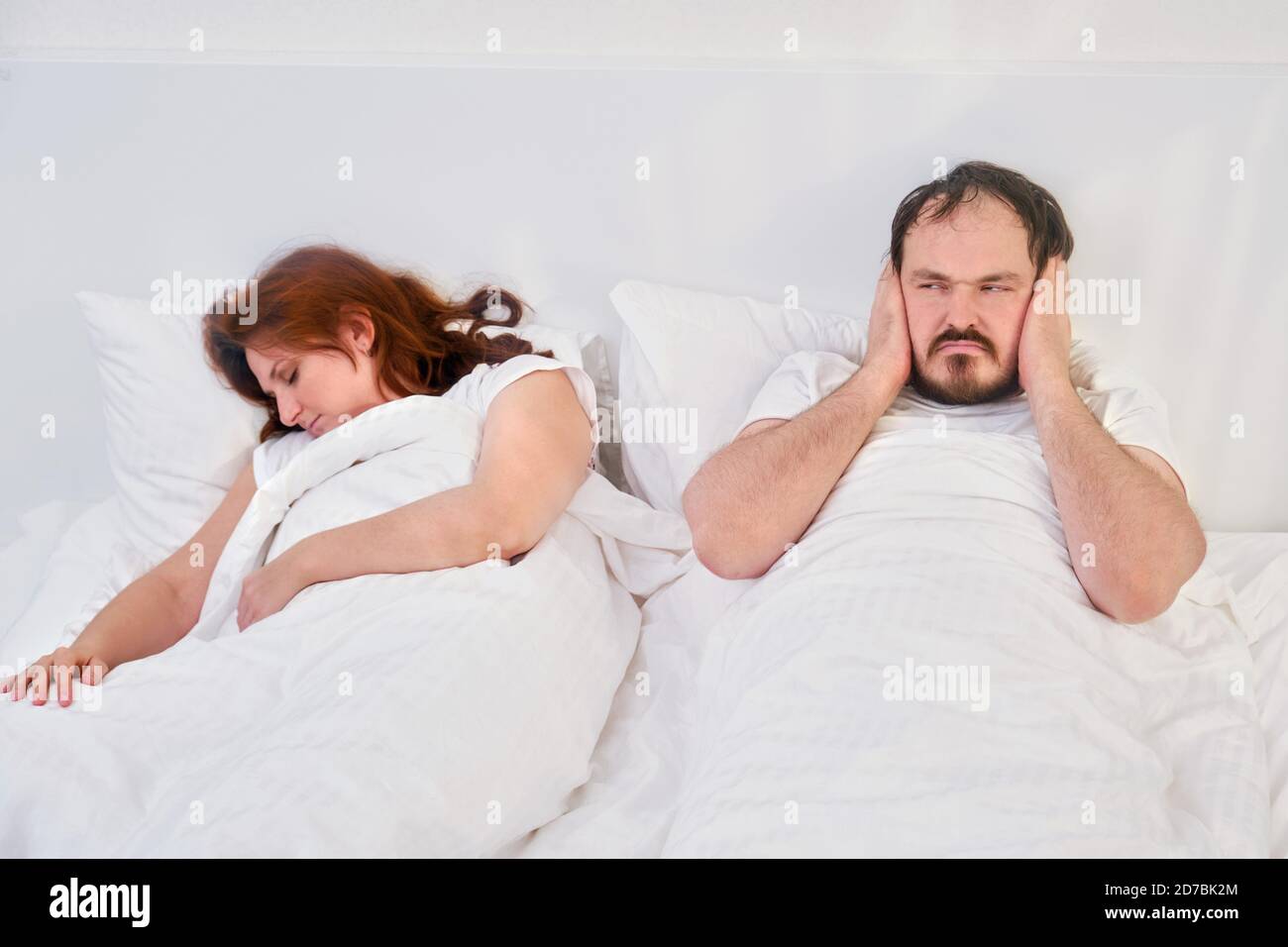 Husband plugs ears with hands due to noise and snoring of sleeping wife. Family relationships in