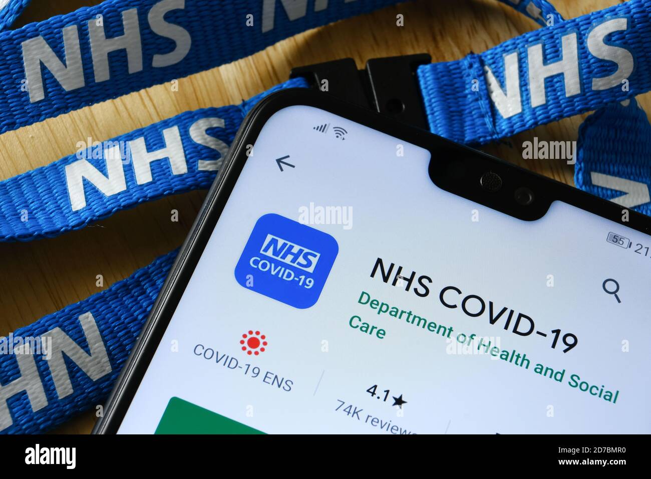 Manchester / United Kingdom - October 21, 2020: NHS COVID-19 app seen in Play Store on the screen of smartphone next to NHS lanyard. Stock Photo