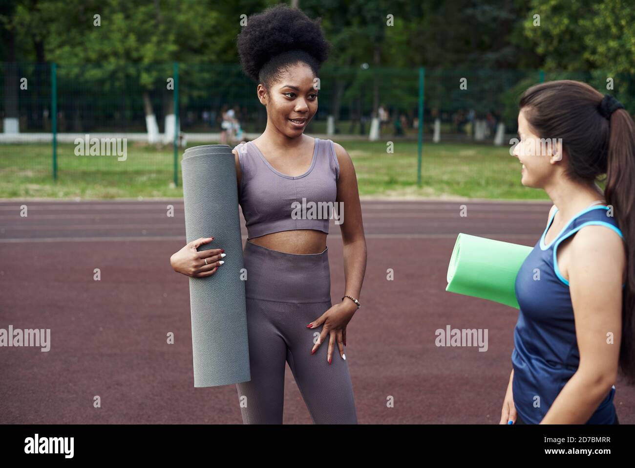 Two sports girls communicate, holding a fitness mat in their hands, on the street. Conversations about sports and fitness. Stock Photo