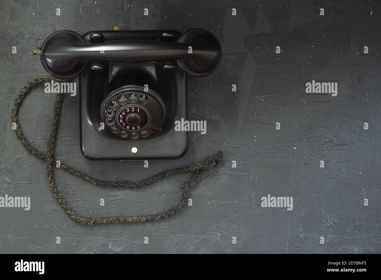 black old telephone receiver hanging on black background with texting space, waiting for phone call, vintage telephone Stock Photo