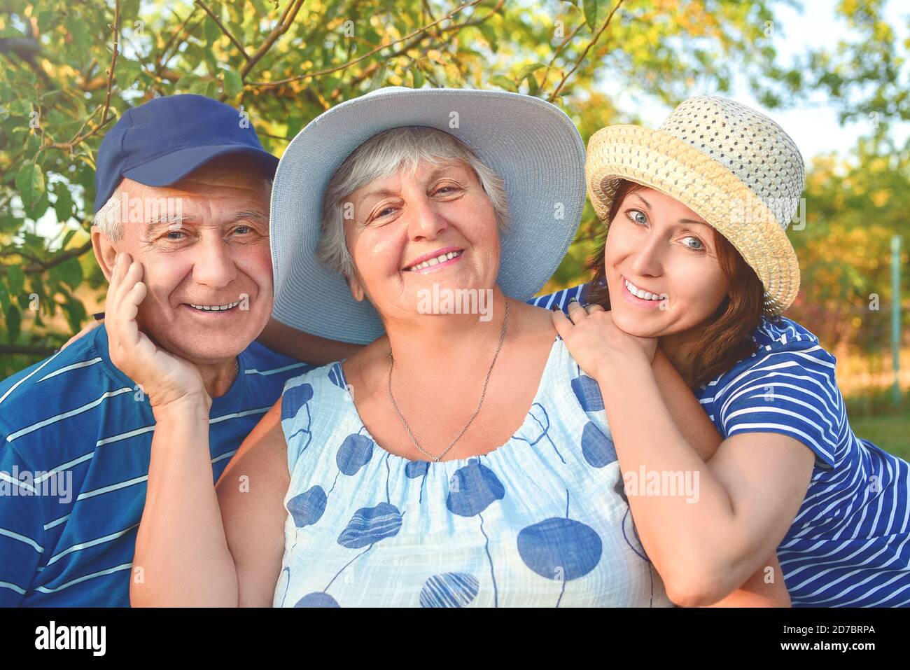 Beautiful senior couple is sitting on the bench in the park with their adult daughter. Grandma and grandpa are hugging and smiling. Real love and fami Stock Photo