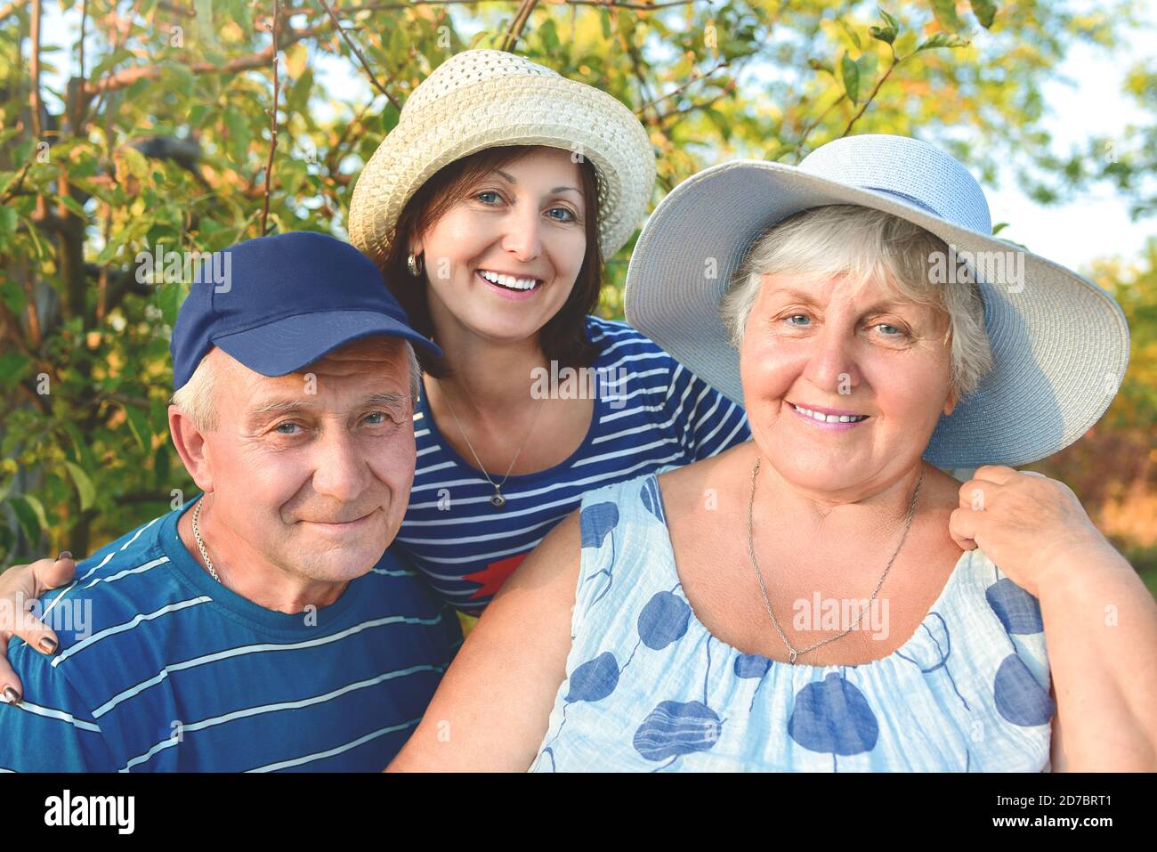 Beautiful senior couple is sitting on the bench in the park with their adult daughter. Grandma and grandpa are hugging and smiling. Real love and fami Stock Photo