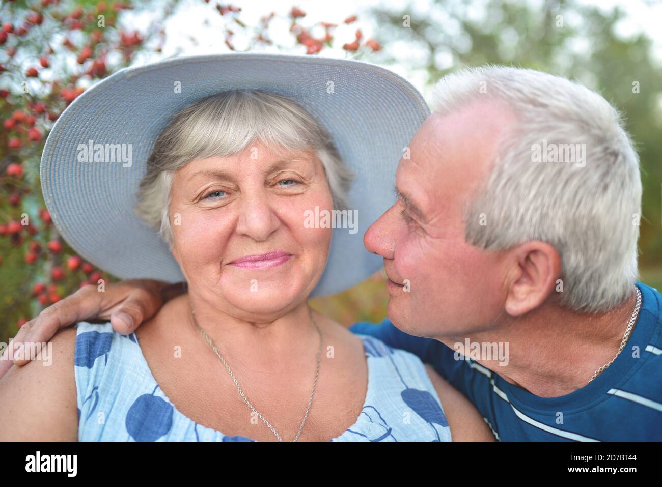 Authentic outdoor shot of aging couple having fun in the garden and blessed with love. During their game man is trying to kiss his wife and she is smi Stock Photo
