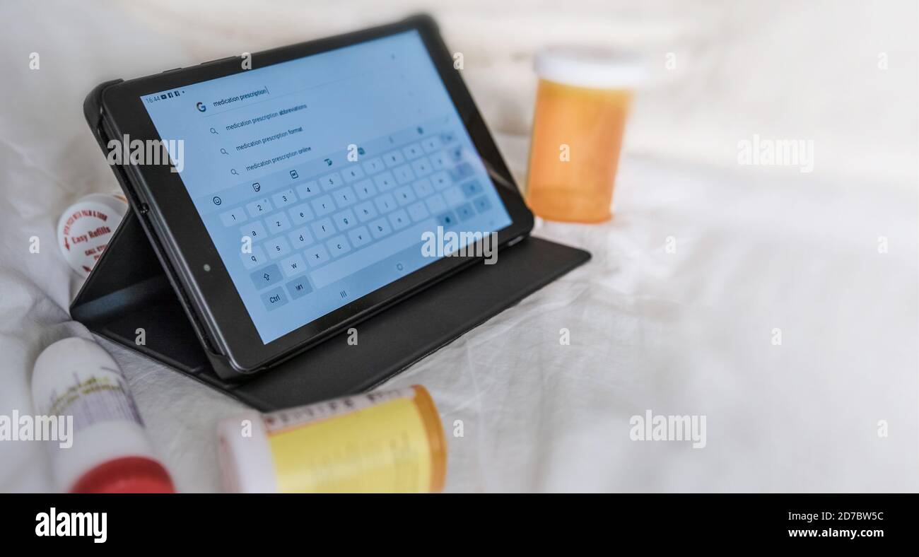 Electronic tablet surrounded by pill containers. Stock Photo