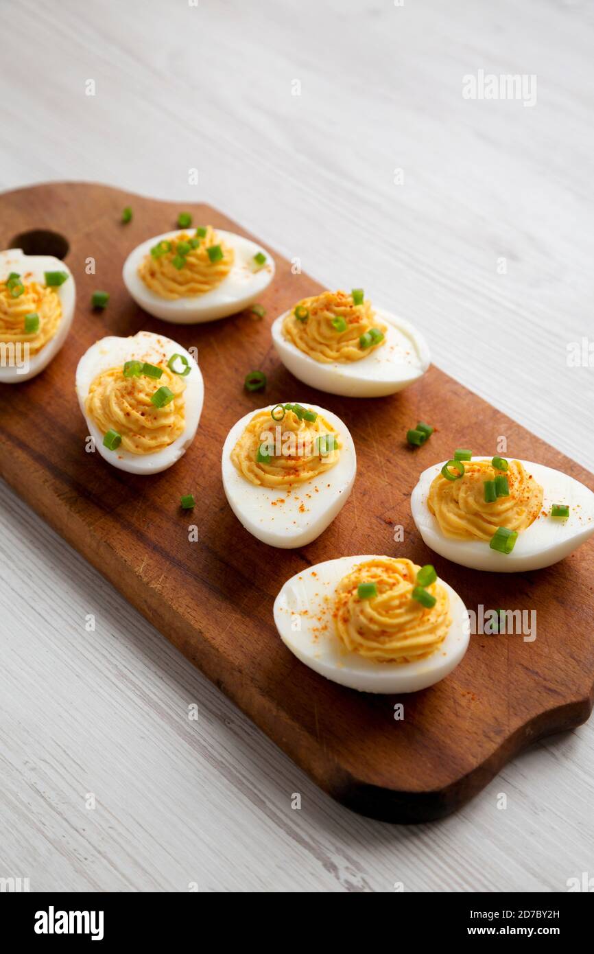 Homemade Deviled Eggs with Chives on a rustic wooden board on a white