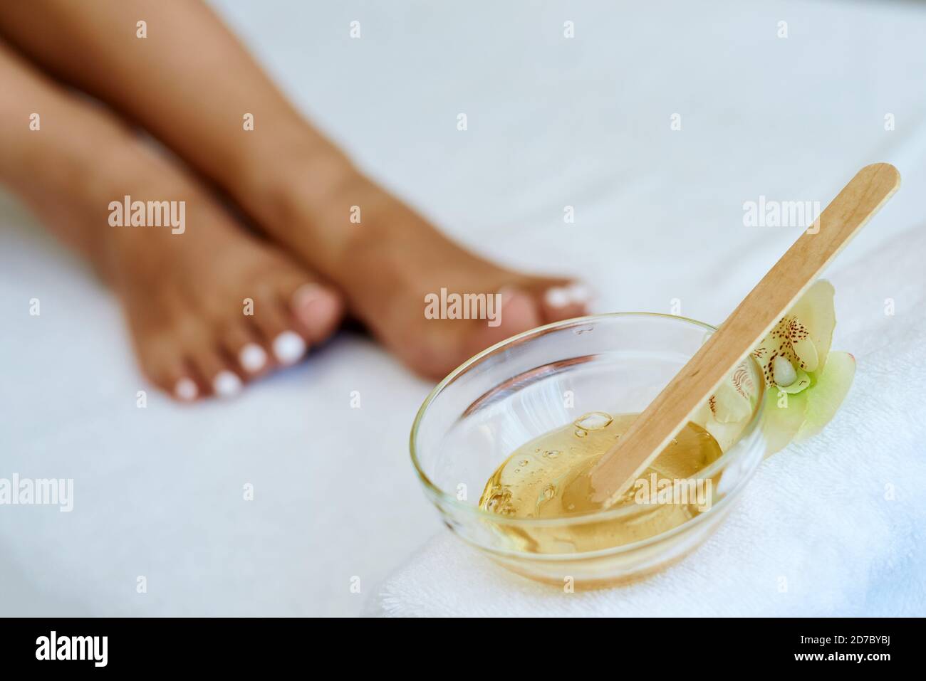 Cosmetologist is doing depilation. The procedures at the beautician. A jar of wax in the foreground. Stock Photo