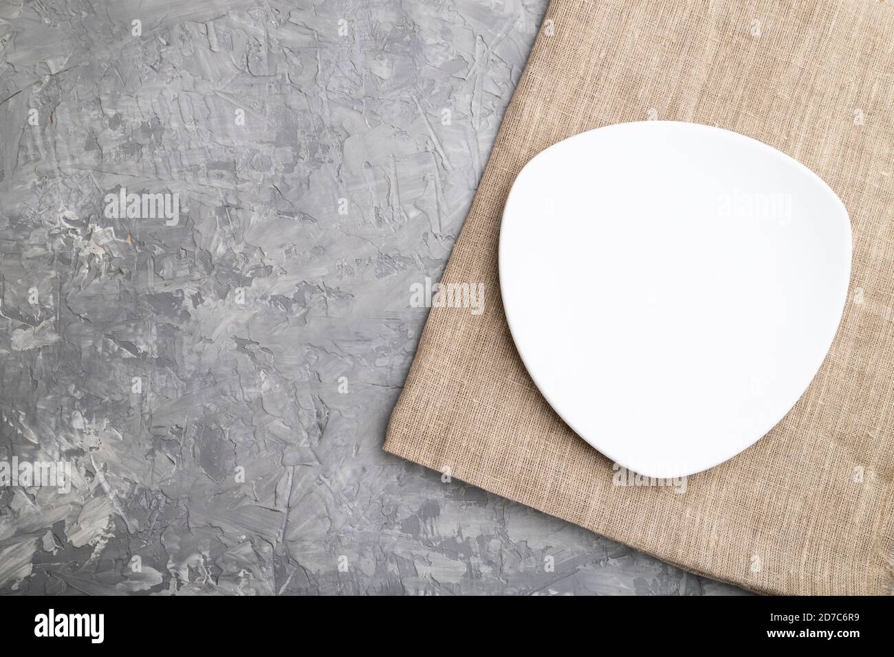 Empty white plate on gray concrete background and linen textile. Top ...