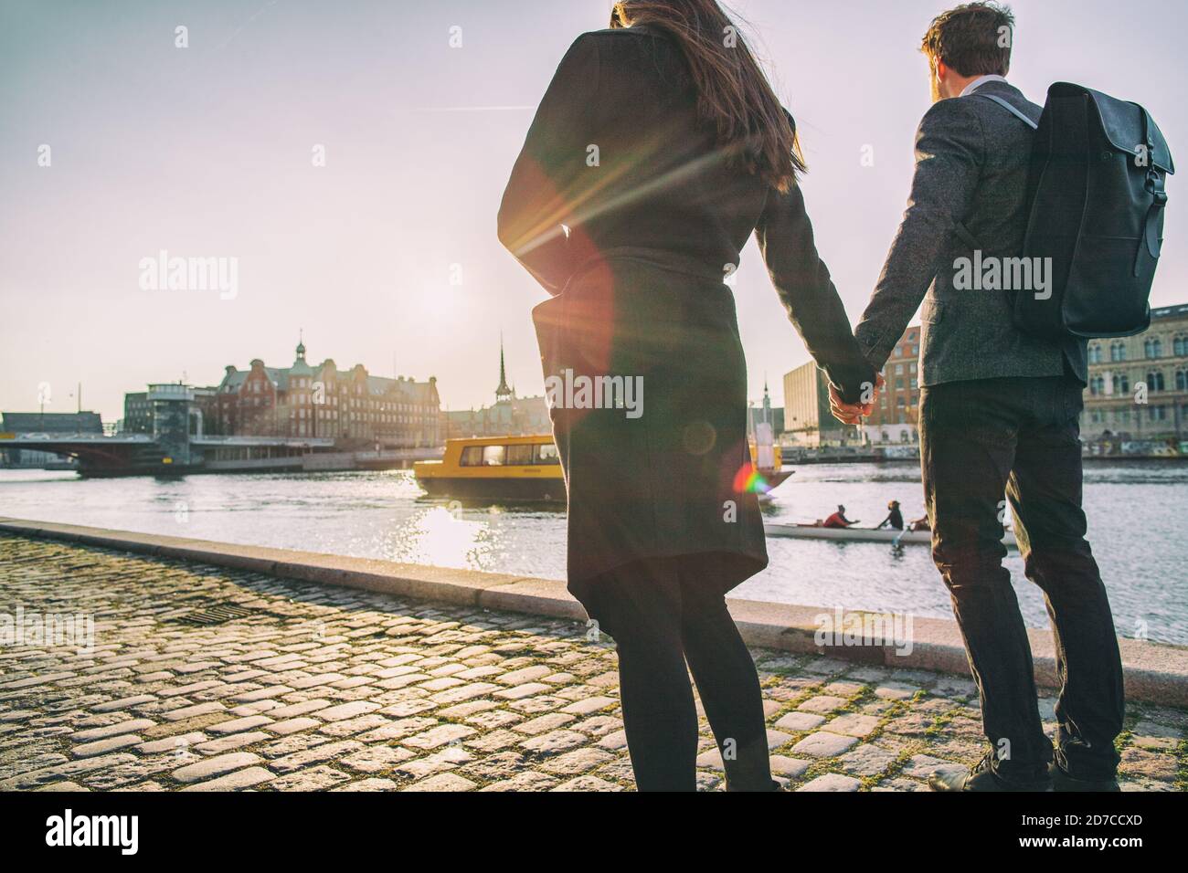 Couple walking on city street at sunset wearing elegant professional coats for fall or autumn. Copenhagen harbour lifestyle young people on outdoor Stock Photo