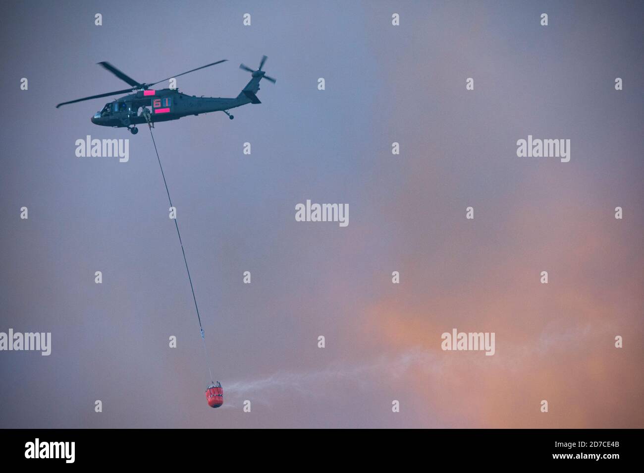 Aerial firefighting helicopter with fire bucket flying into smoke to drop water on wildfire Stock Photo