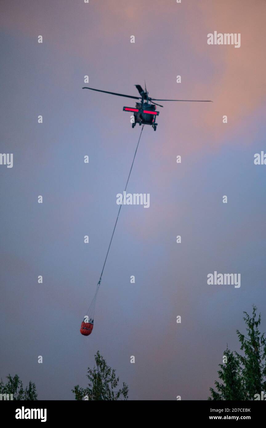 Aerial firefighting helicopter with fire bucket flying into smoke to drop water on wildfire Stock Photo