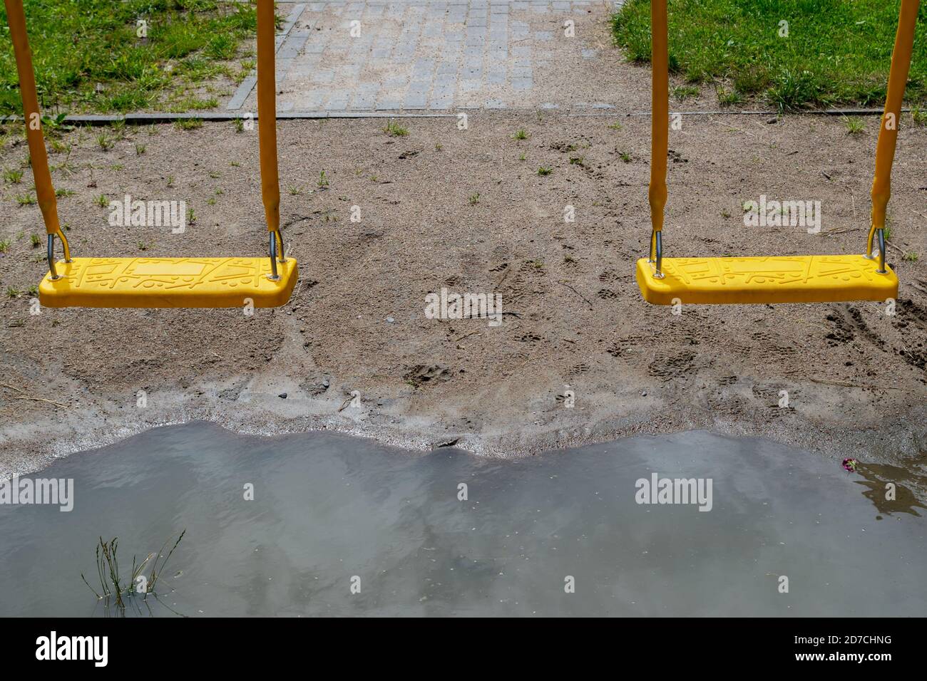 Plastic suspension swings hanging over large puddle after rain, which reflects clouds. Composition against background of sandy soil and paved sidewalk Stock Photo