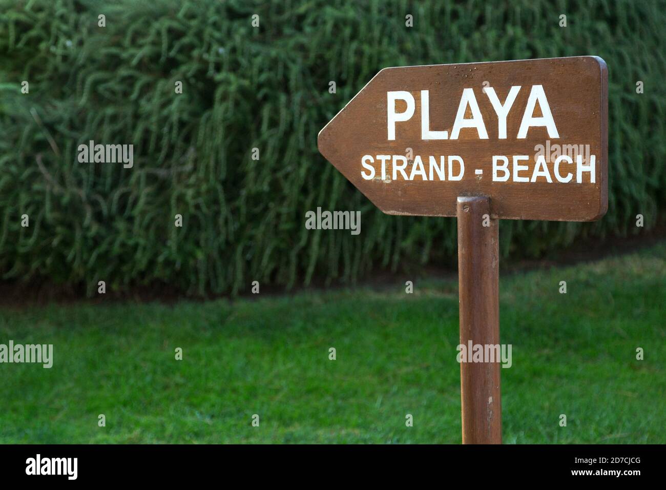 Playa Beach sign in Spanish, English and German. Blurred garden background. Stock Photo