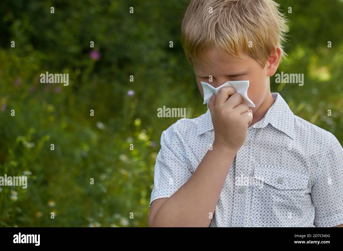 A boy blows his nose in a paper handkerchief on a walk in the Park in summer Stock Photo