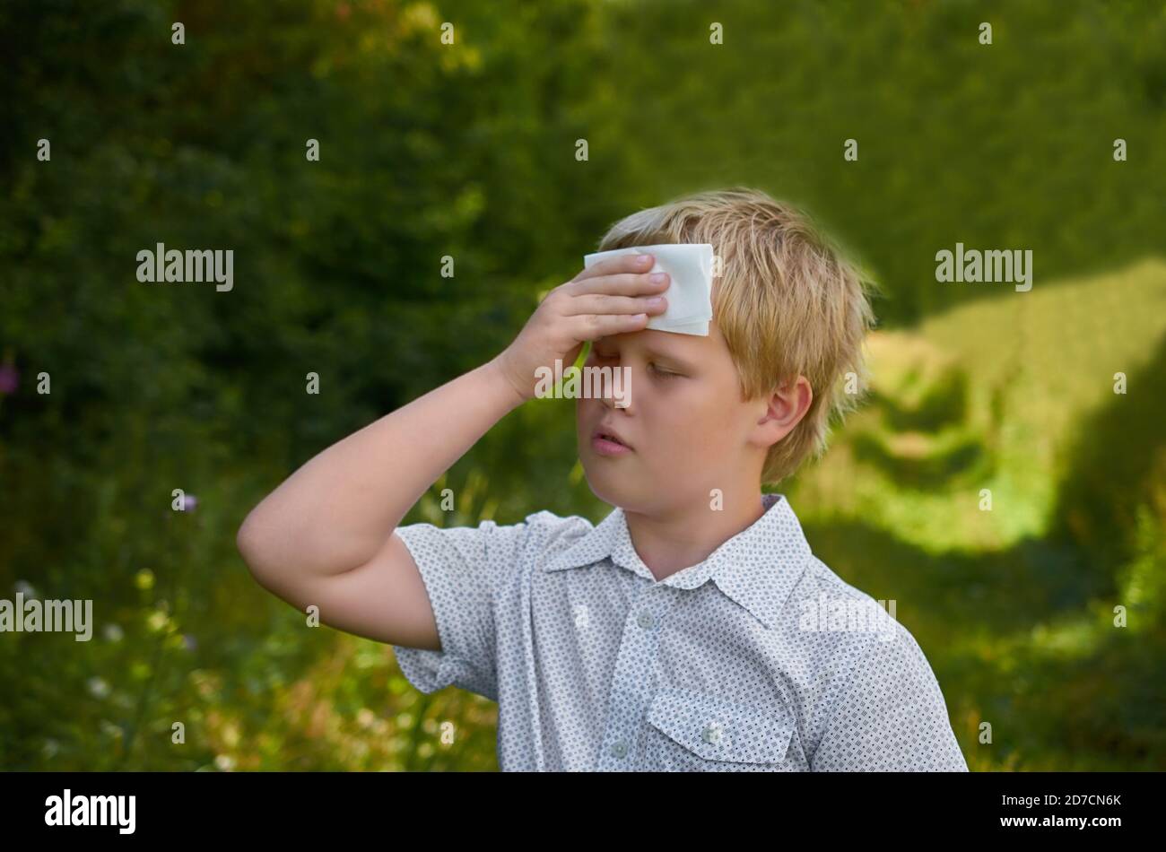 A sad boy wipes his forehead with a paper napkin on a walk in the Park in summer Stock Photo