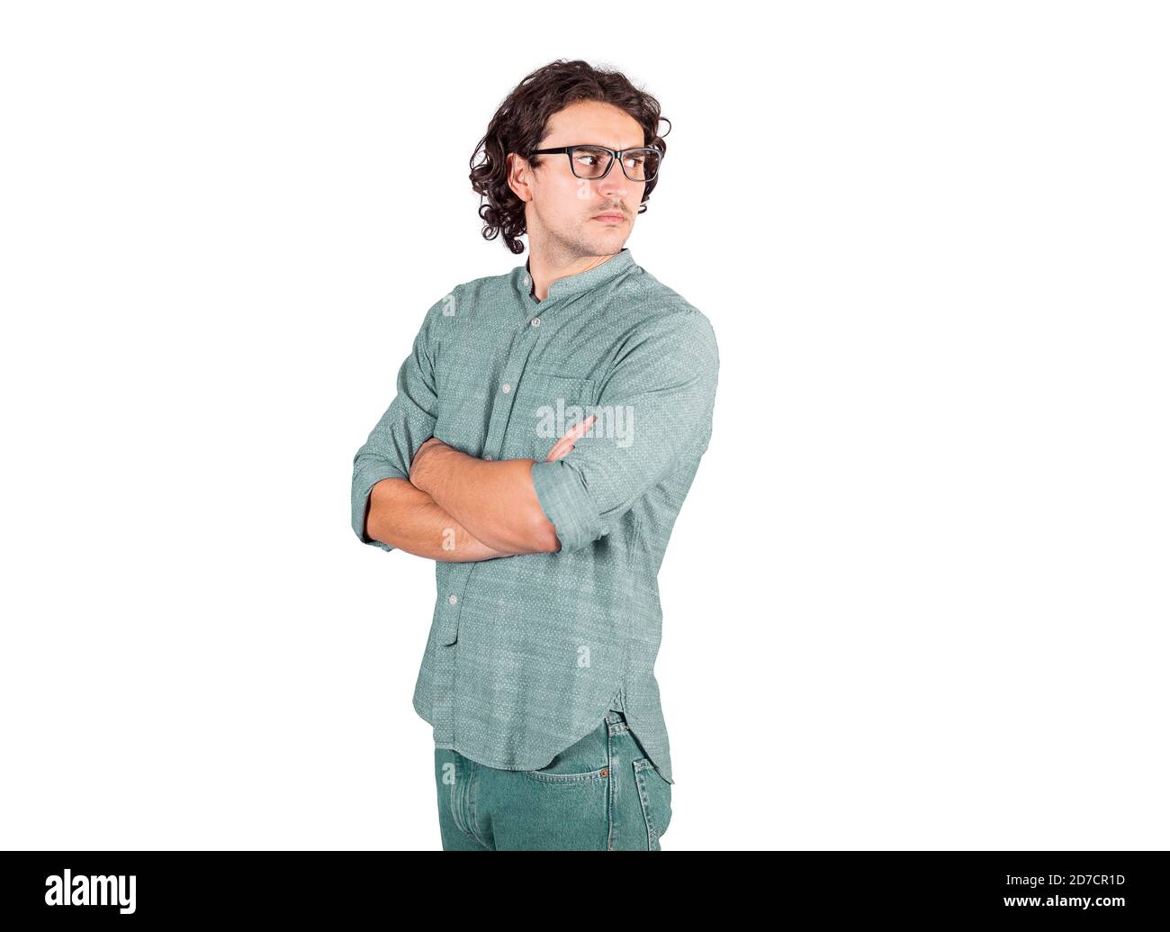 Side view of serious young man, long curly hair style, keeps arms crossed looking confused and bewildered behind his back isolated on white background Stock Photo