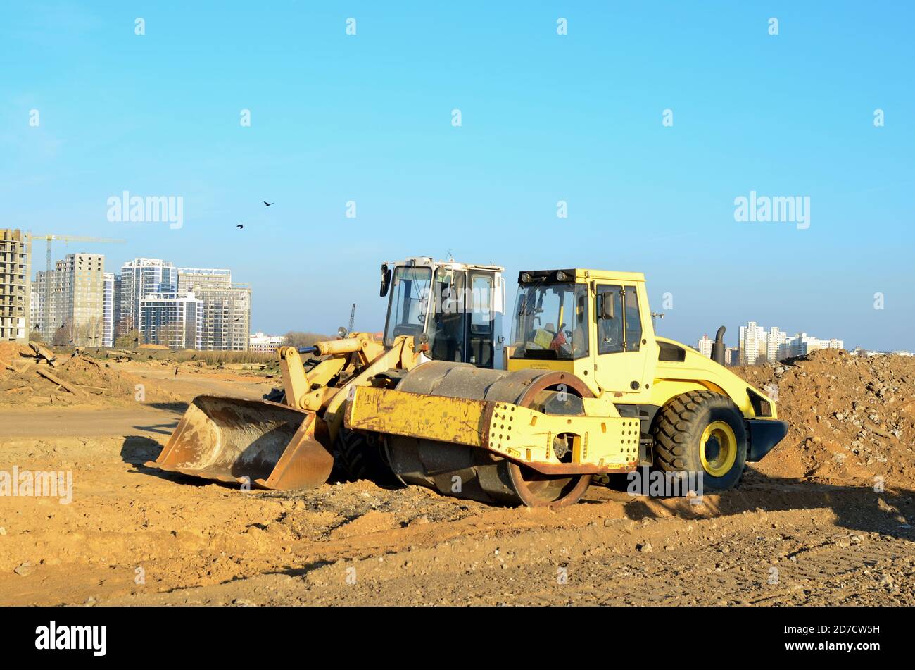 Soil Compactor and wheel loader at construction site. Vibration single-cylinder road roller leveling the ground for the construct of the foundation fo Stock Photo