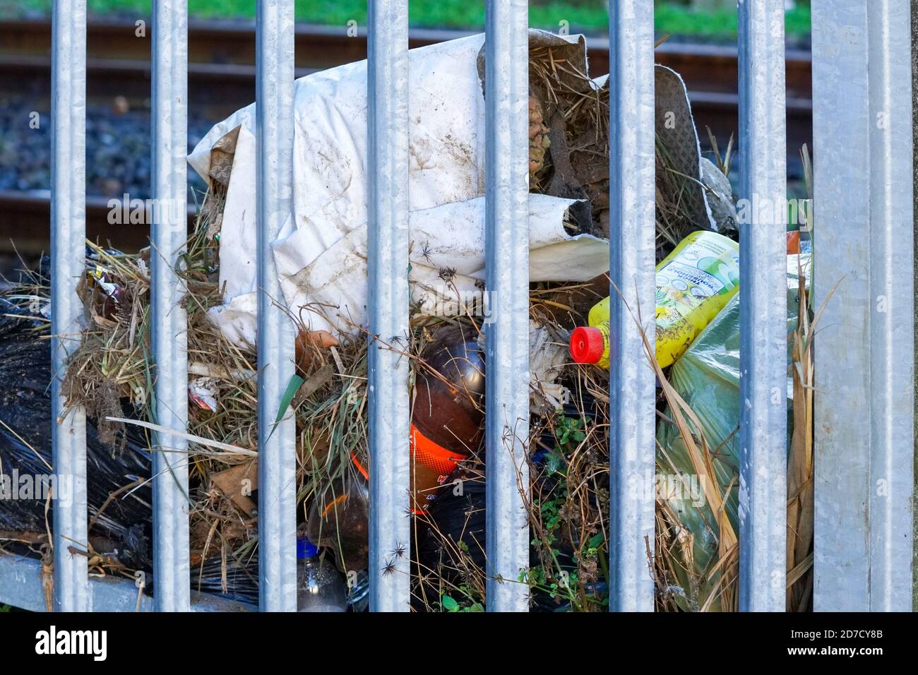 garbage, rubbish, environmental hazard dumped behind fence of a railway line illegally showing damage to the environment Stock Photo