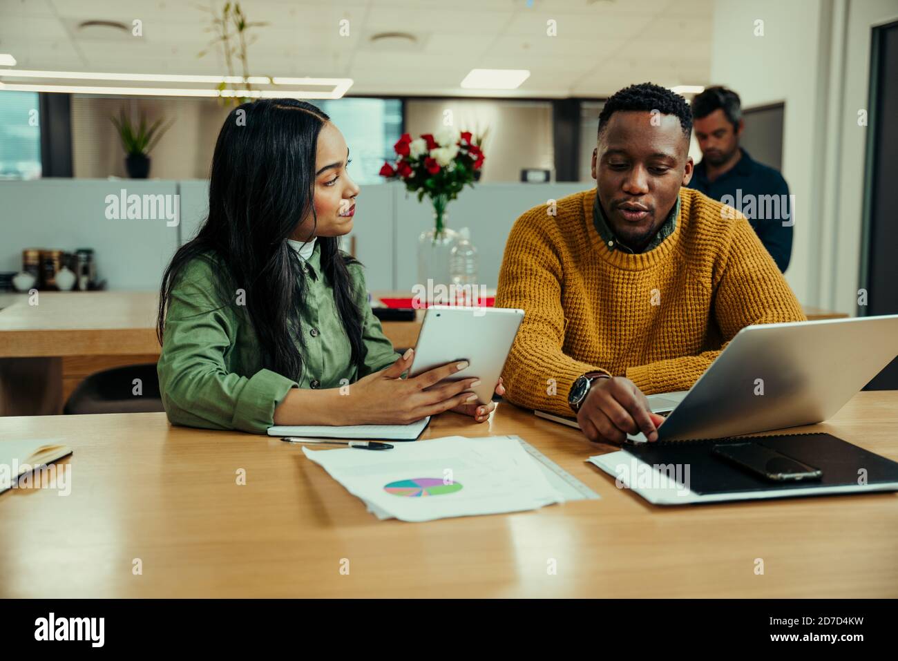 Indian woman working off digital tablet discussing work with mixed race man typing on laptop in office Stock Photo