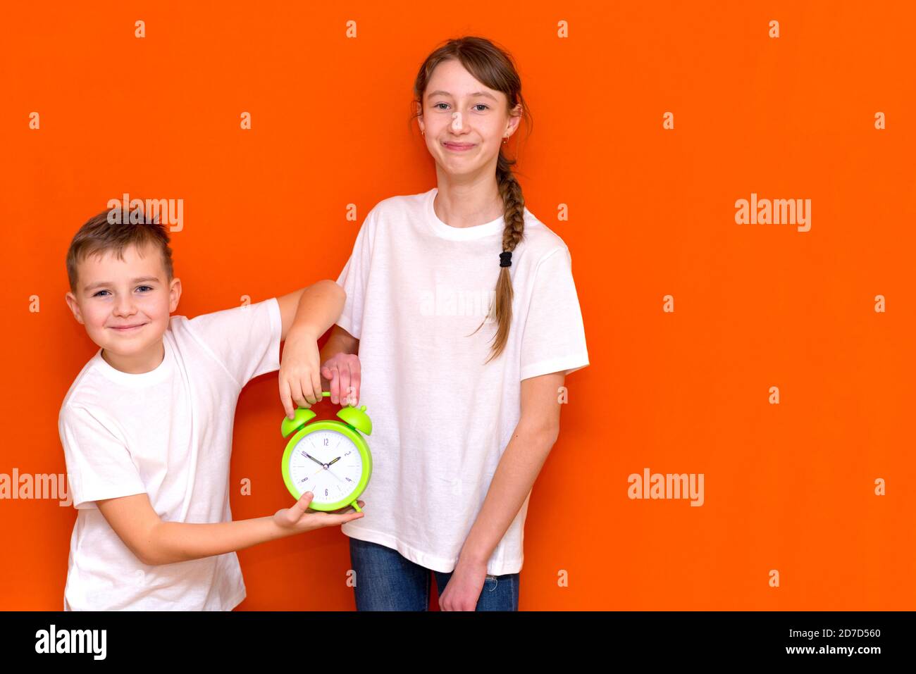 Laughing young caucasians two friends guy and girl in white empty blank design t-shirts posing on orange studio wall. Stock Photo