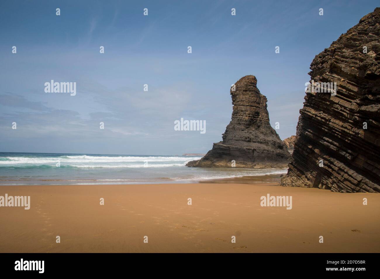 Big and dark schist rock formations standing on beach shore, on a sunny day with clear blue sky Stock Photo