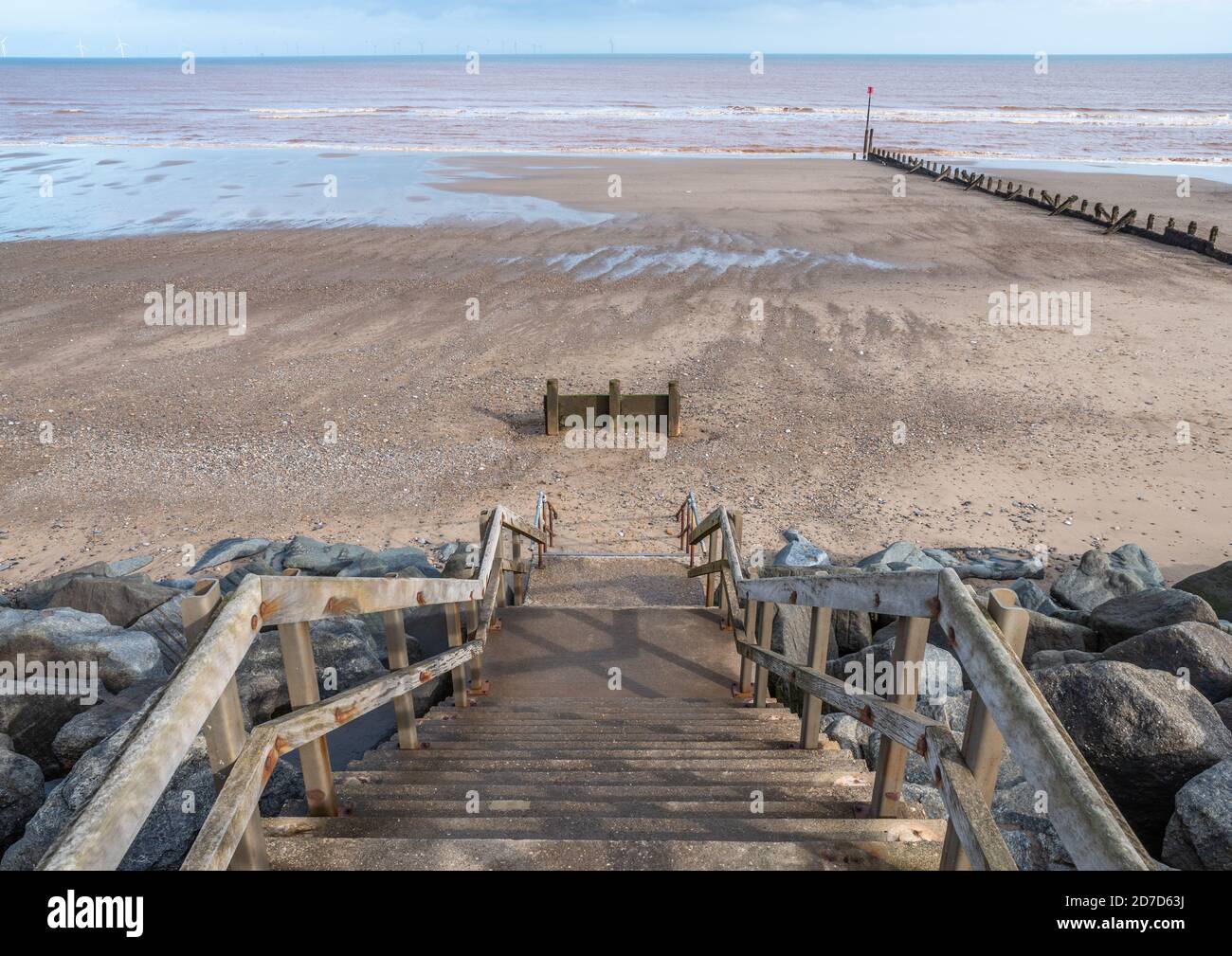 Stairs leading down to a sandy beach with the tide our and the sea in the distance. Stock Photo