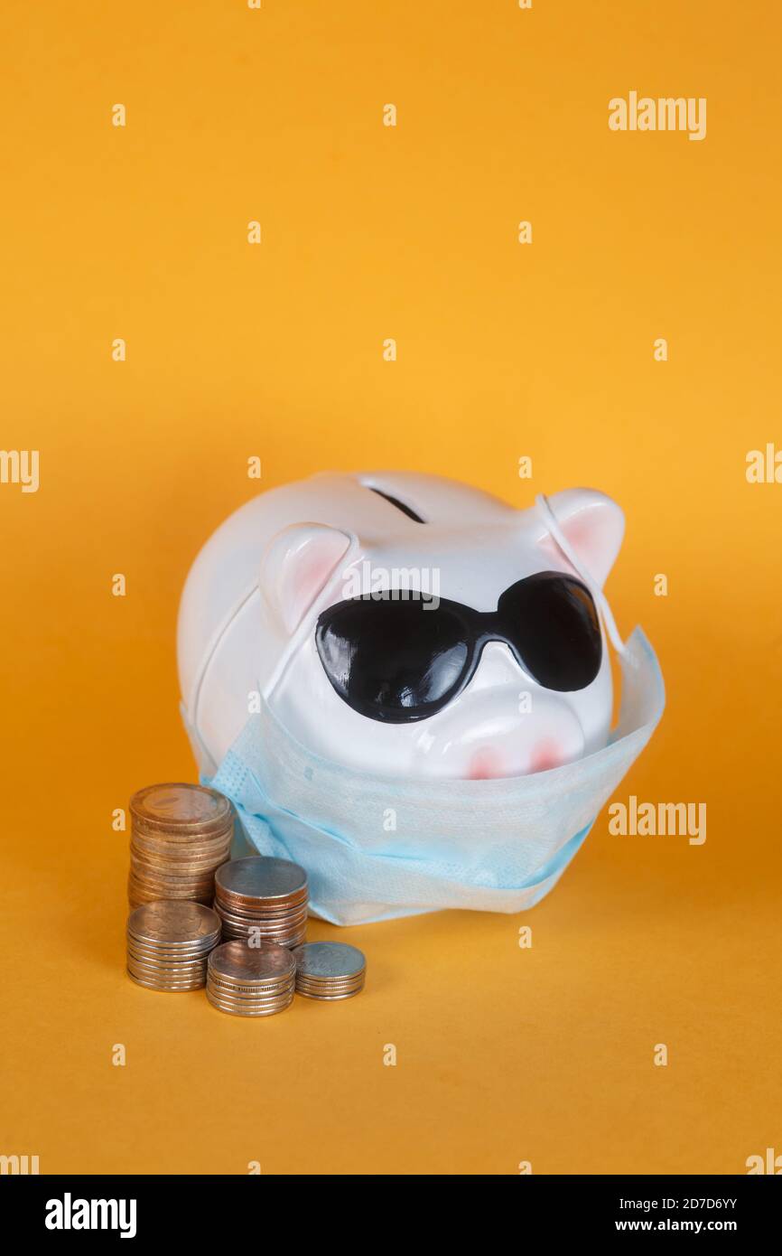 Covid-19 financial crisis. Coronavirus crisis, white piggy bank with face mask stuffed with coin on yellow background. Recession. Stock Photo