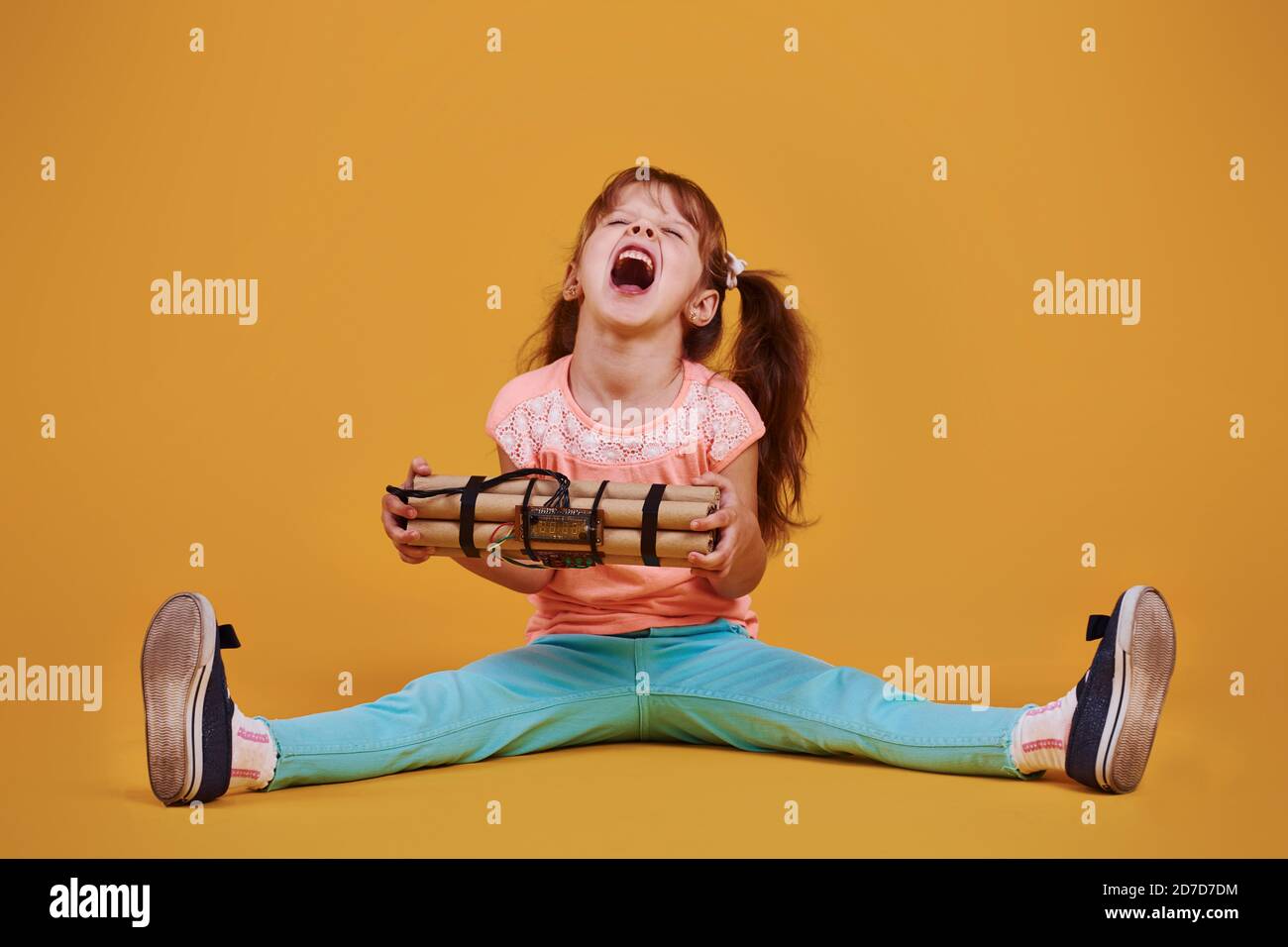 Little girl with explosive in the studio against yellow background ...