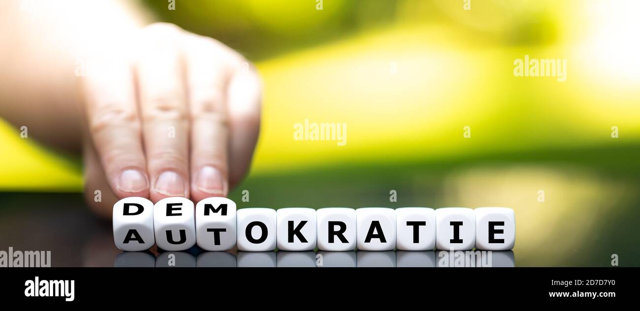 Hand turns dice and changes the German word 'Autokratie' (autocracy) to 'Demokratie' (democracy). Stock Photo