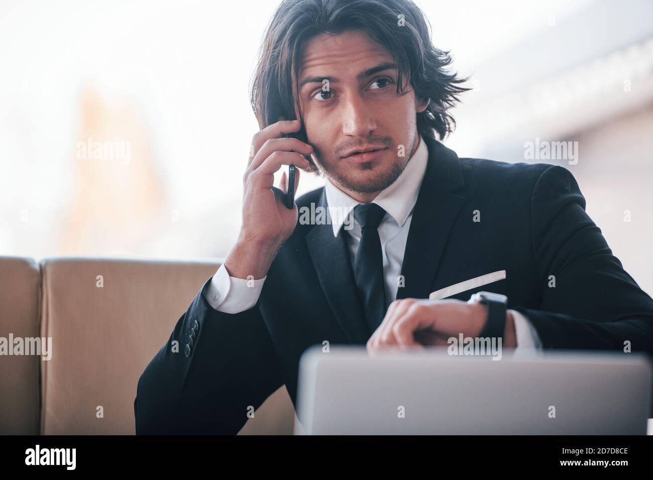 Portrait of handsome young businessman in black suit and tie sits and have a call Stock Photo