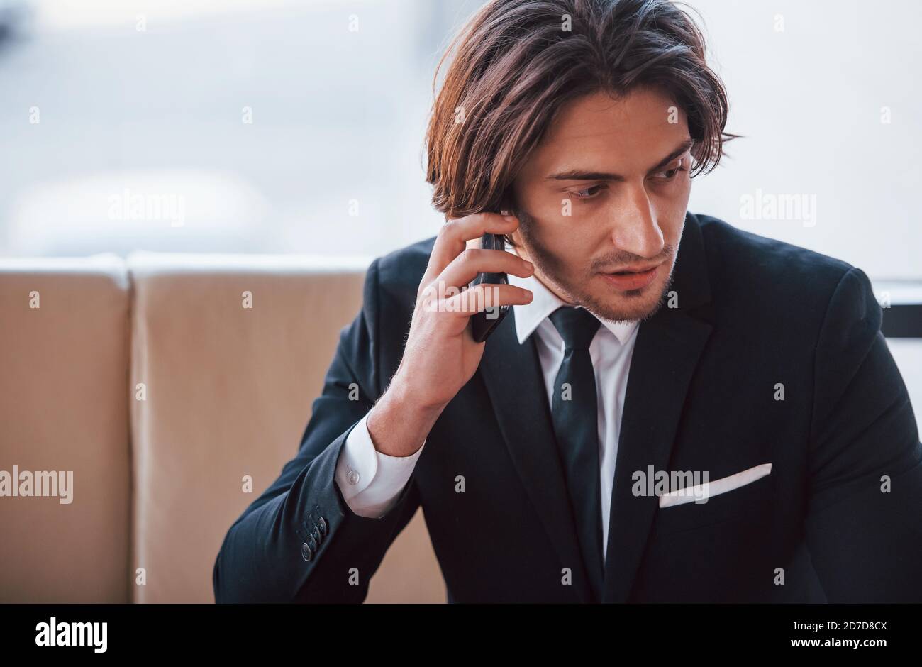 Portrait of handsome young businessman in black suit and tie sits and have a call Stock Photo