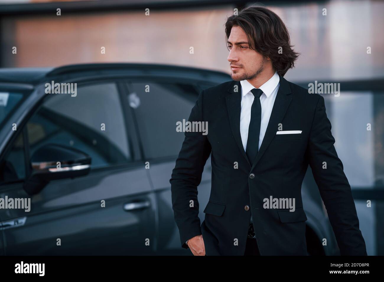 Portrait of handsome young businessman in black suit and tie outdoors ...