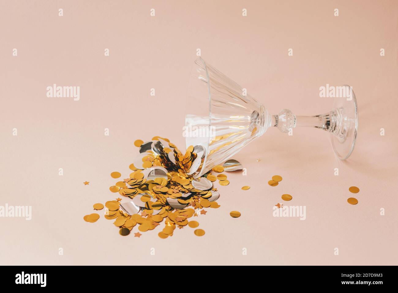 Wine glass with gold sparkles or confetti on a pink background