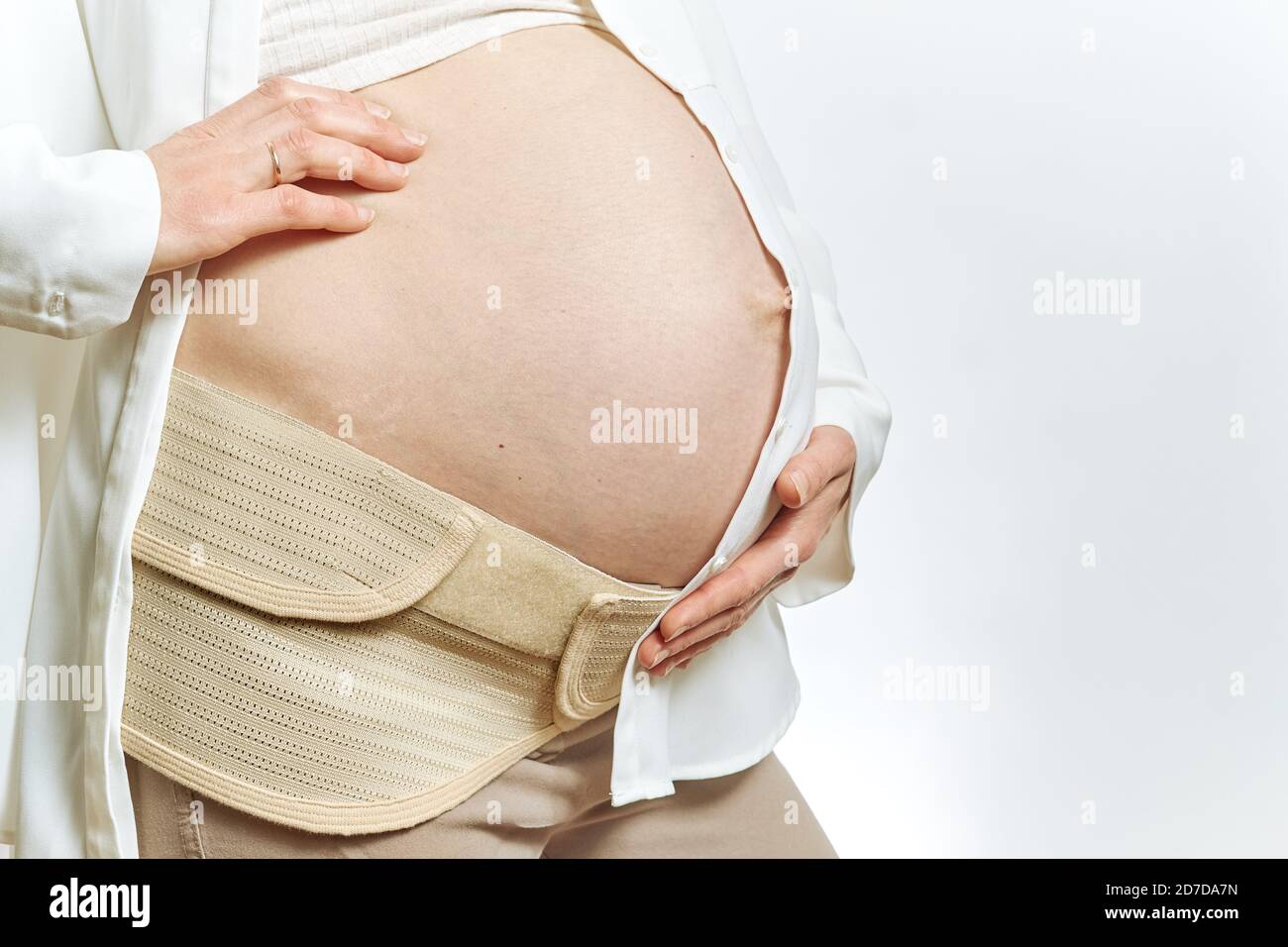 Pregnant woman's belly faceless and hands close-up isolated. Maternity Belt Pregnancy Abdomen Support Abdominal Binde. side view and copy space. Stock Photo