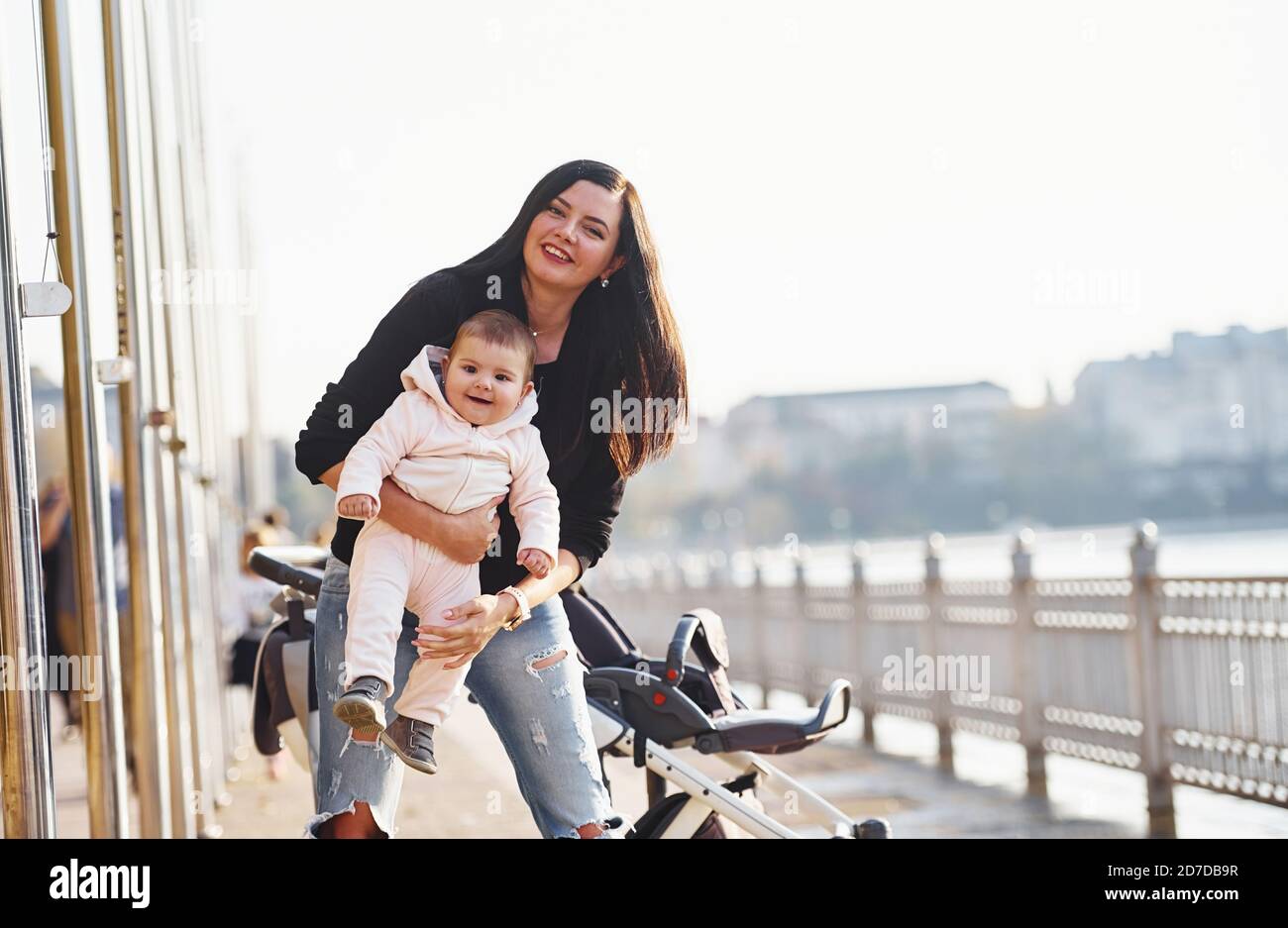 Mother with pram in casual clothes with her child is in the park Stock Photo