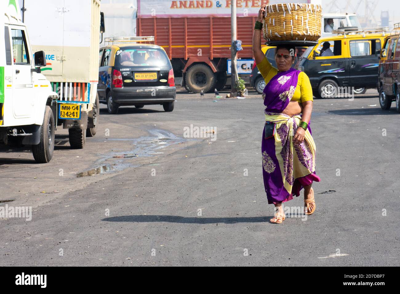 Mumbai, India - March 23, 2019: Mid-aged woman in traditional saree carrying a bamboo basket on her head and crossing near St.Michael's Church. Stock Photo