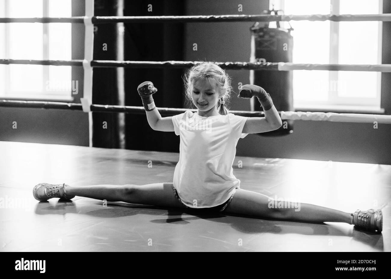 Black and white photo. Young little girl in sportive wear is in the gym have exercise day. Conception of boxing Stock Photo