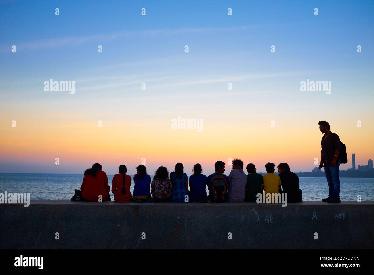 During sunset over the Arabian Sea at Marine Drive, near Chowpatty Beach, Mumbai, a group of sightseers enjoy the view while sitting on the embankment Stock Photo