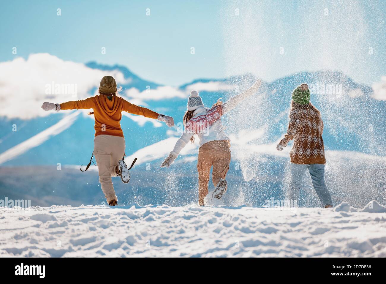 Three happy adult girls are having fun, runs and throwing snow in mountains. First snow concept Stock Photo
