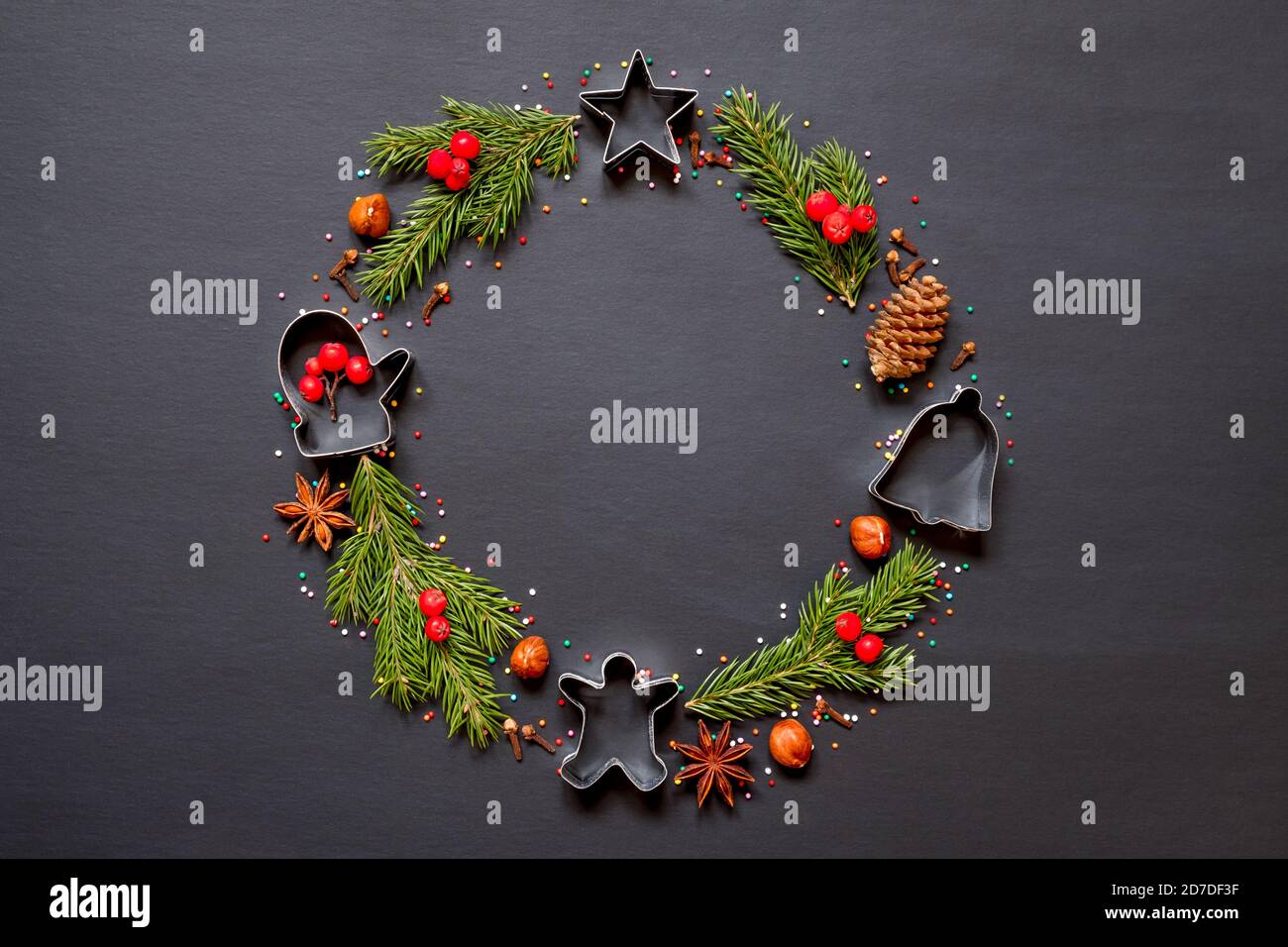 Christmas wreath made from molds for cookies, spices and a Christmas tree on a black background with copy space. Stock Photo
