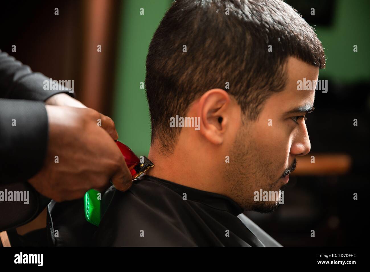 A black African-American barber cuts and shaves the hair of a Hispanic ...