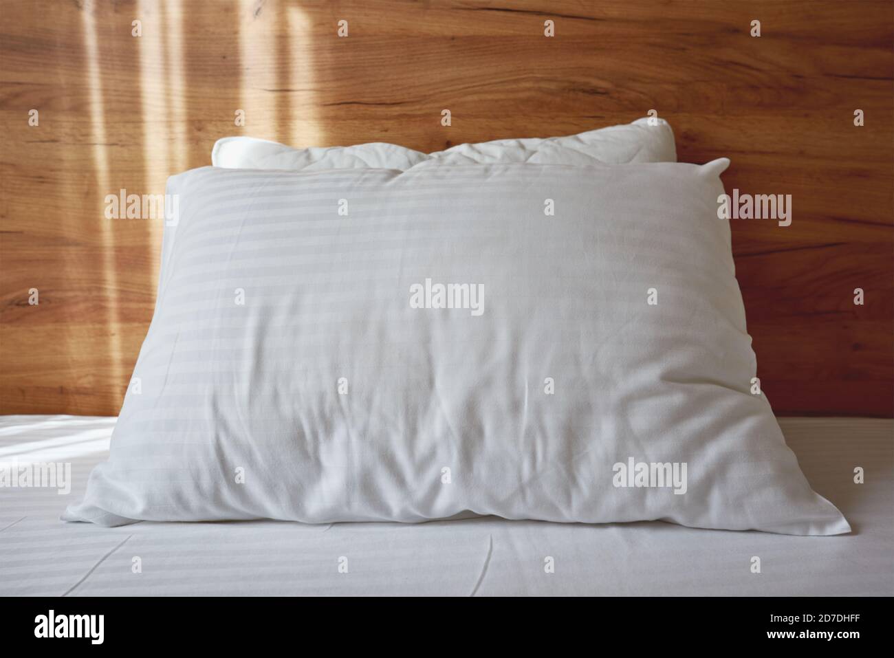 White pillow on bed in apartment bedroom with morning sunlight beaming through curtains Stock Photo